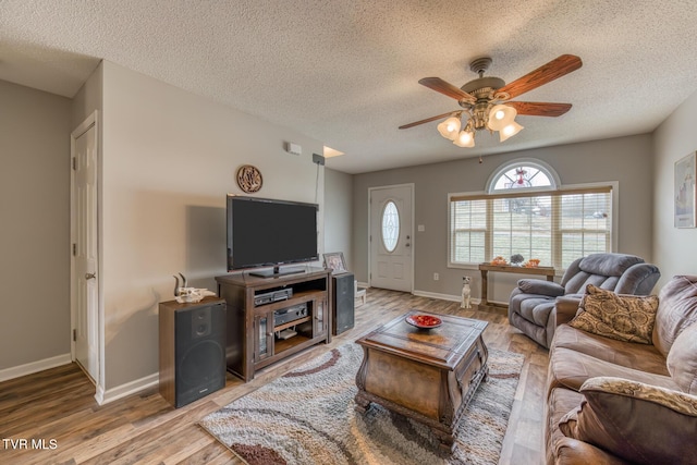 living area with light wood-type flooring, baseboards, a textured ceiling, and ceiling fan