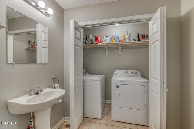 washroom with a sink, light tile patterned flooring, baseboards, laundry area, and washing machine and clothes dryer