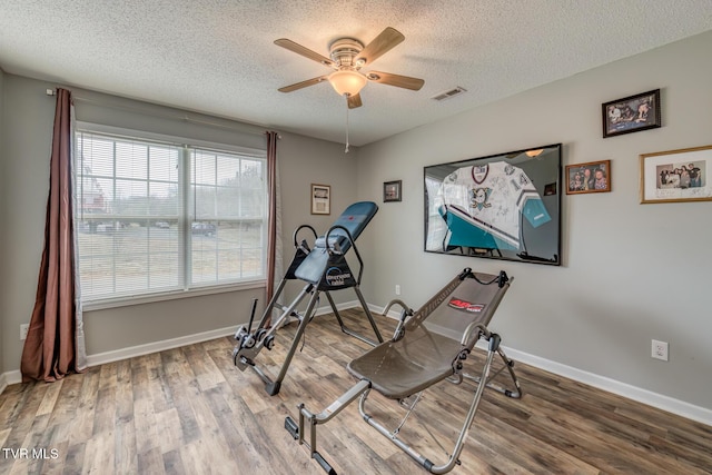 workout area featuring visible vents, a textured ceiling, baseboards, and wood finished floors