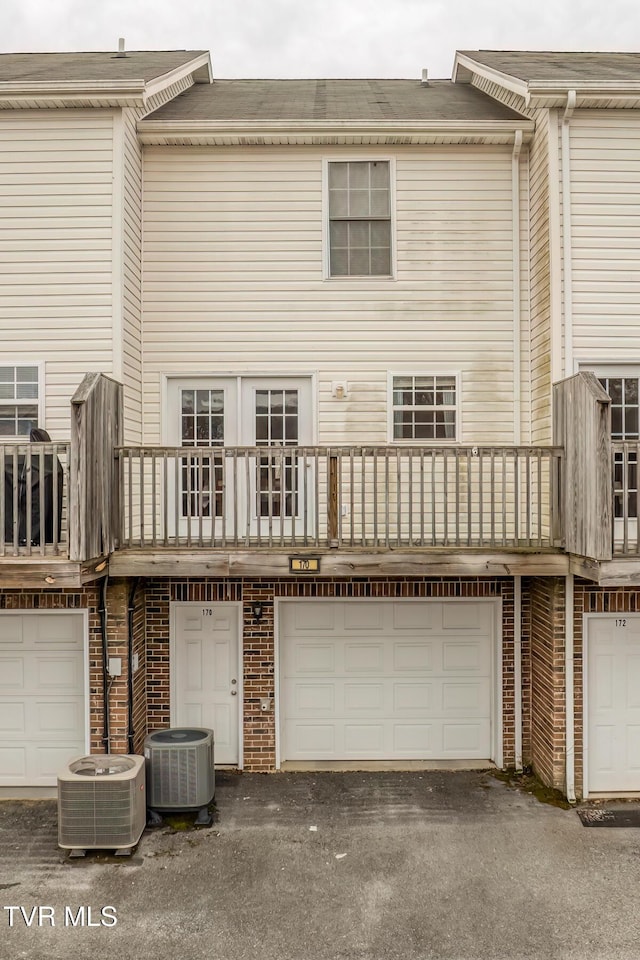 rear view of property featuring cooling unit, an attached garage, and aphalt driveway