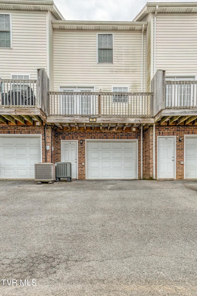 back of property featuring brick siding, cooling unit, an attached garage, and driveway