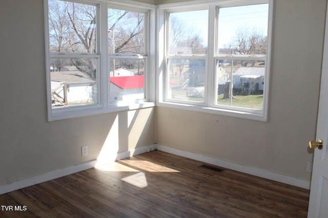 unfurnished room featuring visible vents, plenty of natural light, baseboards, and wood finished floors