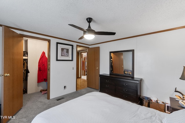 carpeted bedroom with a spacious closet, visible vents, a textured ceiling, and ornamental molding