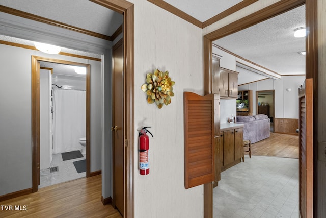 corridor with a textured ceiling, light wood-style floors, and ornamental molding