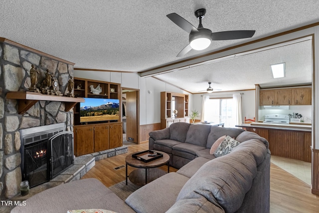 living area featuring lofted ceiling with beams, a textured ceiling, light wood-style flooring, and a fireplace