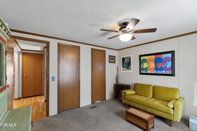 living area with ceiling fan, a textured ceiling, ornamental molding, and carpet