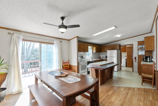 dining area featuring light wood-type flooring, ornamental molding, a textured ceiling, washer / dryer, and vaulted ceiling