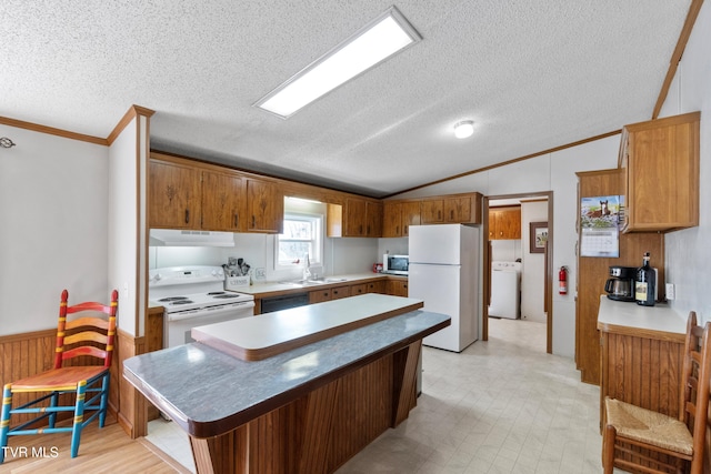 kitchen featuring a wainscoted wall, under cabinet range hood, a sink, white appliances, and lofted ceiling