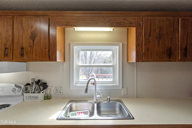 kitchen with electric range, brown cabinets, light countertops, and a sink