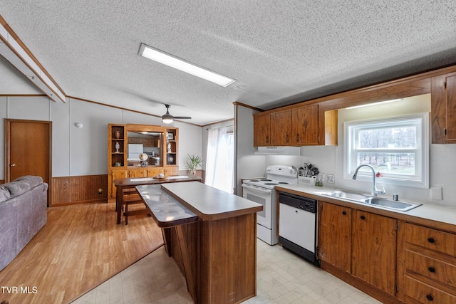 kitchen featuring white appliances, brown cabinetry, light floors, a kitchen island, and a sink