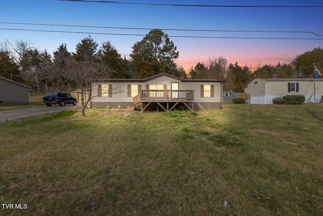 manufactured / mobile home with aphalt driveway, a wooden deck, and a front yard