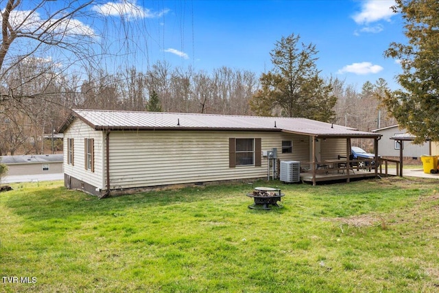 back of property with an outdoor fire pit, a lawn, metal roof, a deck, and crawl space