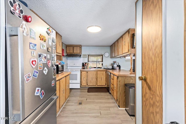 kitchen featuring light countertops, appliances with stainless steel finishes, light wood-style floors, a textured ceiling, and a sink