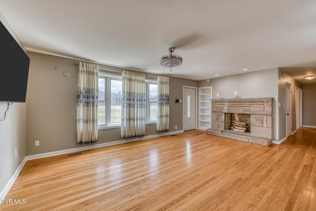 unfurnished living room featuring a stone fireplace, visible vents, wood finished floors, and baseboards