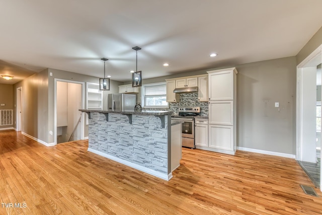 kitchen featuring visible vents, light wood-type flooring, decorative backsplash, appliances with stainless steel finishes, and a kitchen breakfast bar