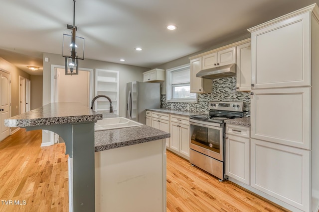 kitchen featuring an island with sink, a sink, stainless steel appliances, under cabinet range hood, and tasteful backsplash