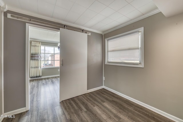 empty room with a barn door, baseboards, crown molding, and dark wood-type flooring