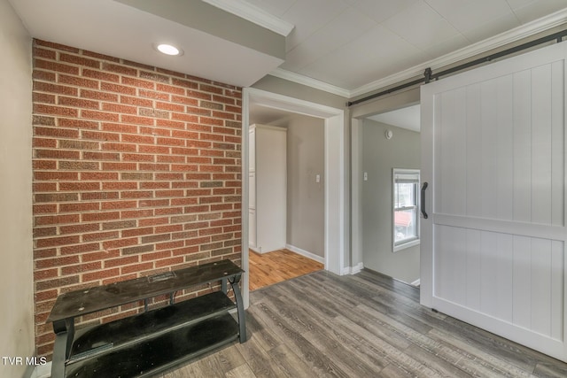 unfurnished living room featuring brick wall, baseboards, a barn door, ornamental molding, and wood finished floors