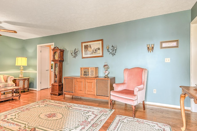 living area featuring baseboards, a textured ceiling, wood finished floors, and a ceiling fan