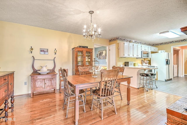 dining space with light wood finished floors, a textured ceiling, and an inviting chandelier