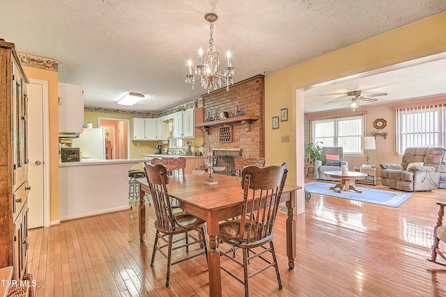 dining area featuring light wood finished floors, ceiling fan with notable chandelier, a textured ceiling, and baseboards