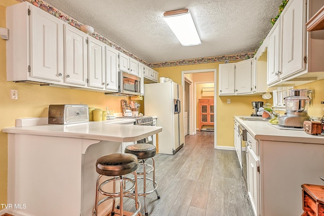 kitchen featuring light wood finished floors, stainless steel microwave, white cabinetry, and white fridge with ice dispenser