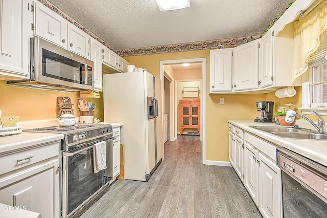 kitchen featuring light wood-style flooring, a sink, white cabinetry, appliances with stainless steel finishes, and light countertops