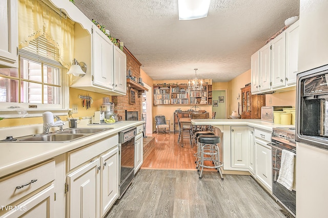 kitchen with light wood finished floors, dishwasher, range, white cabinets, and a sink