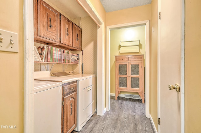 laundry area with washer and clothes dryer, a textured ceiling, cabinet space, light wood finished floors, and baseboards