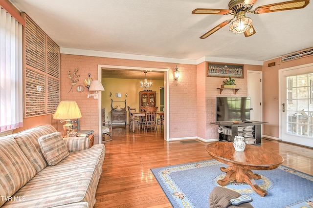 living area featuring ceiling fan with notable chandelier, brick wall, and hardwood / wood-style flooring