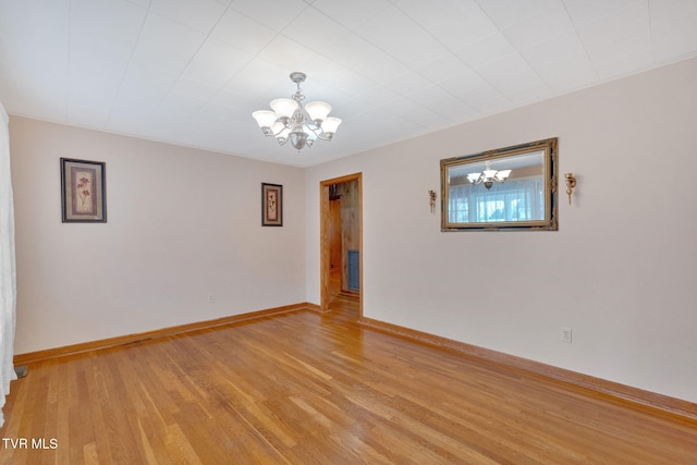 spare room featuring light wood-style flooring, baseboards, and a chandelier