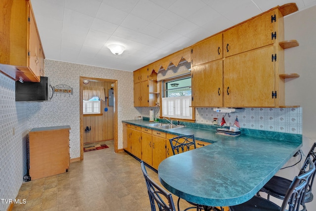 kitchen with baseboards, wallpapered walls, a peninsula, a sink, and dark countertops