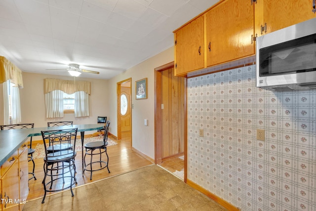 kitchen with a ceiling fan, stainless steel microwave, brown cabinetry, and baseboards