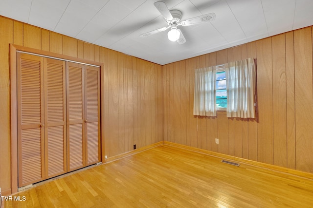 unfurnished bedroom featuring visible vents, ceiling fan, wood walls, wood finished floors, and a closet