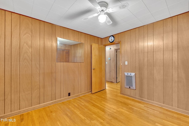 spare room featuring wooden walls, baseboards, ceiling fan, wood finished floors, and heating unit