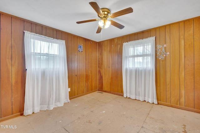 unfurnished room with wooden walls, ceiling fan, and baseboards