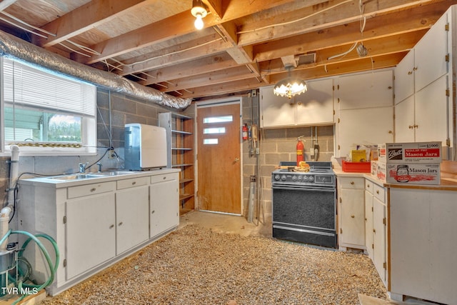 kitchen with a sink, white cabinetry, concrete block wall, light countertops, and black range with gas cooktop