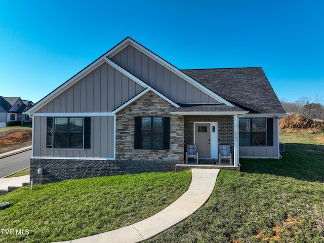 view of front of property featuring stone siding, roof with shingles, board and batten siding, and a front lawn