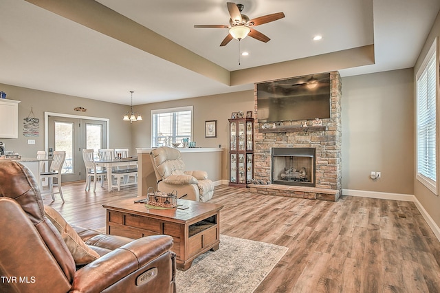 living area featuring baseboards, a raised ceiling, light wood-style floors, and a fireplace