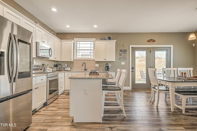 kitchen with a center island, a kitchen bar, stainless steel appliances, wood finished floors, and white cabinetry