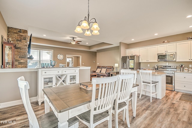 dining room with recessed lighting, a tray ceiling, light wood-style floors, and a ceiling fan