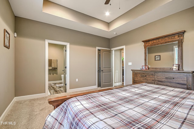 bedroom featuring a tray ceiling, connected bathroom, baseboards, and carpet