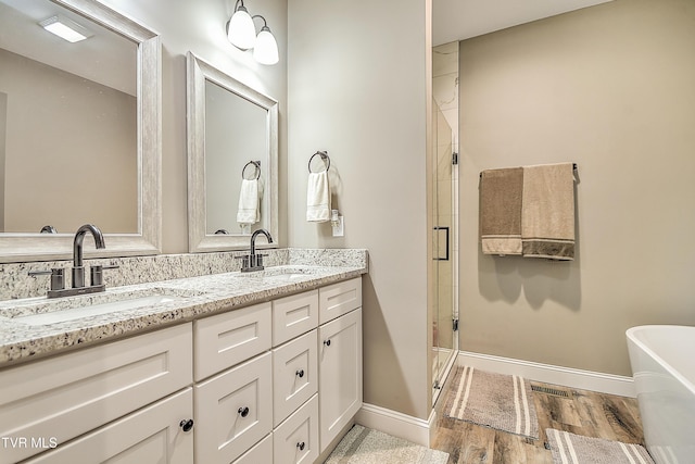 bathroom with a sink, wood finished floors, a stall shower, and double vanity