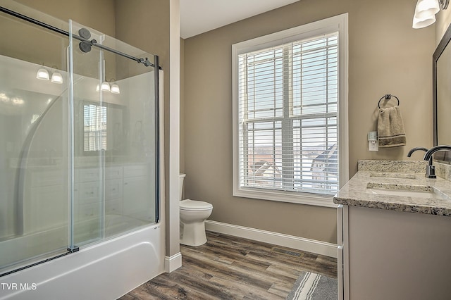 bathroom with baseboards, toilet, double vanity, wood finished floors, and a sink