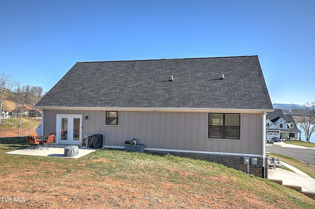 rear view of property with french doors, a lawn, a shingled roof, and a patio area