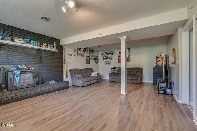 living area with a wood stove, wood finished floors, visible vents, and a textured ceiling