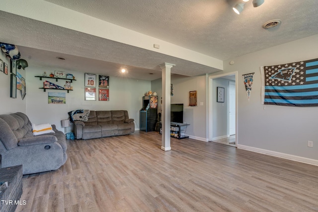 living room with wood finished floors, baseboards, visible vents, ornate columns, and a textured ceiling