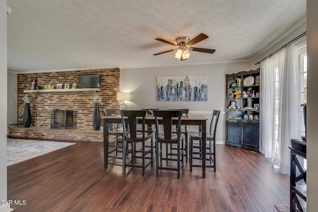 dining area featuring a fireplace, a textured ceiling, crown molding, and wood finished floors