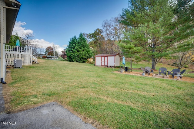 view of yard with a shed, a wooden deck, central AC, an outdoor structure, and a fire pit