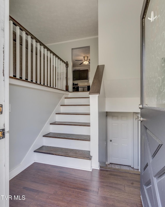 stairs with wood finished floors, a ceiling fan, and crown molding